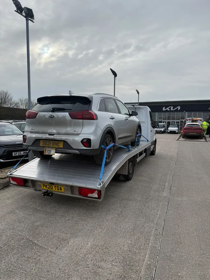 KCS Recovery truck loaded with a silver Kia Niro at a Kia main dealership