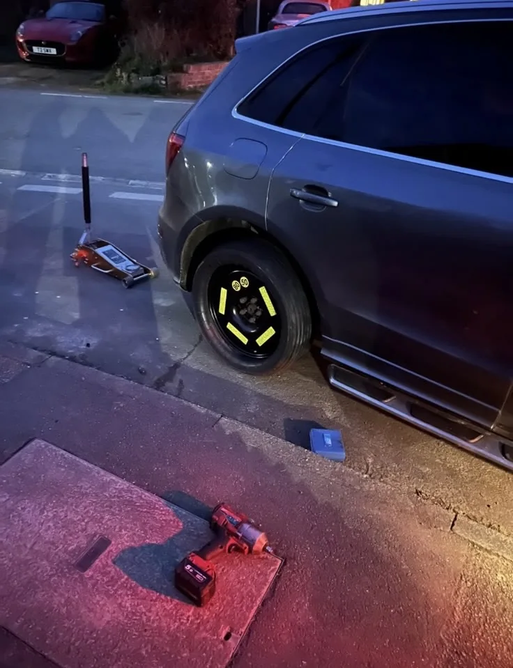 Spare wheel fitted at the roadside on a jacked up car at dusk in Kent